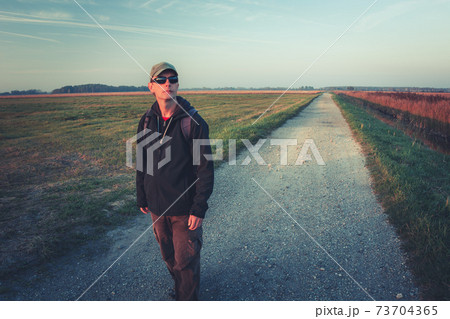 A man in sunglasses with a backpack goes the gravel road A man in sunglasses with a backpack goes the gravel road 73704365