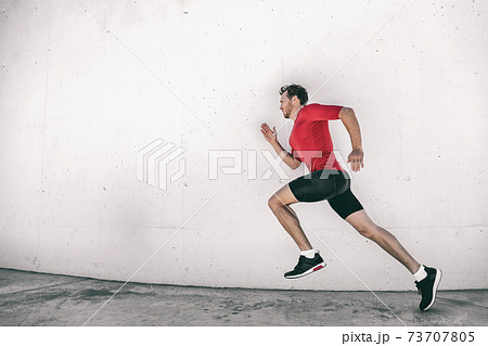 Running man fit athlete male runner working out outside doing city street run sprinting along gym wall. Sprinter going fast living active lifestyle doing sprint hiit high intensity interval training 73707805