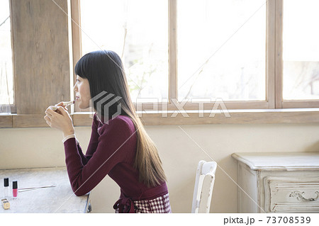 椅子に座って窓際で口紅を塗る女性 椅子に座って窓際で口紅を塗る女性 73708539