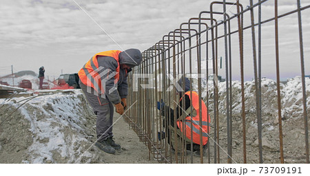 Engineers work with metal constructions while building a house. Builder fixes armature while working on construction site. Workers at joining metallic iron bars structure for reinforcement wall 73709191