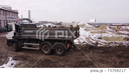 Upper aerial shot: a tractor bucket fills the truck body. An excavator and a truck load the ground. Flight over the construction site where workers are pouring the foundation. Lots of equipment 73709217