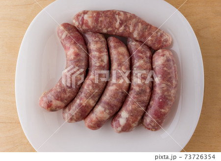 Raw sausages for a barbecue on a white plate. Several barbecue sausages lie next to each other. Raw sausages for a barbecue on a white plate. Several barbecue sausages lie next to each other. 73726354