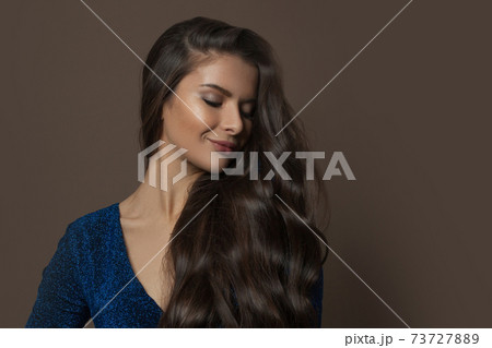 Fashionable brunette model woman with long curly hair on brown background, fashion beauty portrait 73727889