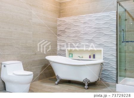 White and wooden bathroom corner with a white bathtub, a toilet and a built in shelf for self care products White and wooden bathroom corner with a white bathtub, a toilet and a built in shelf for self care products 73729228