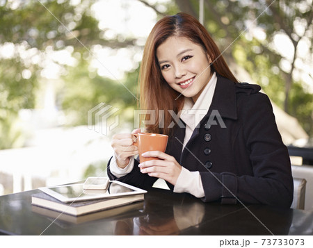 young asian adult woman holding coffee cup looking at camera smiling in cafe 73733073