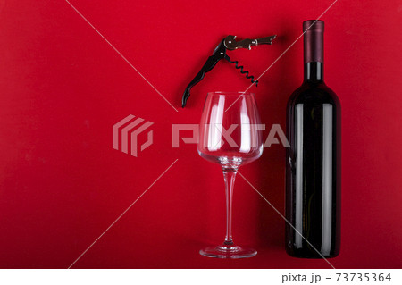 Bottle of red wine and an empty wine glass with a corkscrew next to it. Composition on a red background. Romantic mood. Space for text. Bottle of red wine and an empty wine glass with a corkscrew next to it. Composition on a red background. Romantic mood. Space for text. 73735364