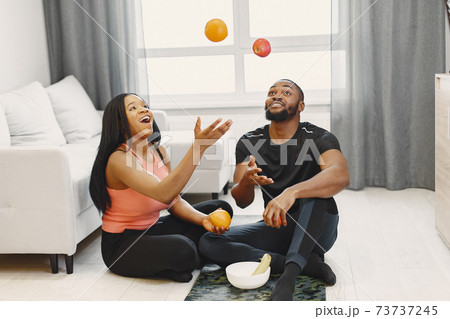 Handsome Afro American couple sitting with fruitsat home Handsome Afro American couple sitting with fruitsat home 73737245
