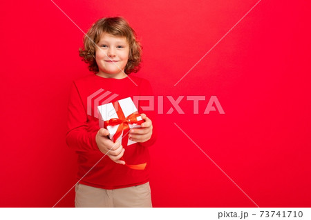 Photo shot of joyful smiling blonde curly boy isolated over red background wall wearing red sweater 73741710
