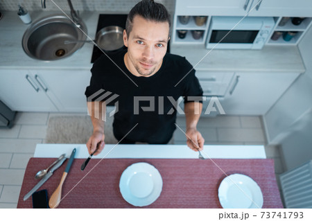 attractive hungry young man on modern kitchen with empty plate, fork and knife 73741793
