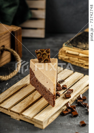 Still life of chestnut cake with chocolate mousse on a dark gray table with chocolate pieces. 73742748