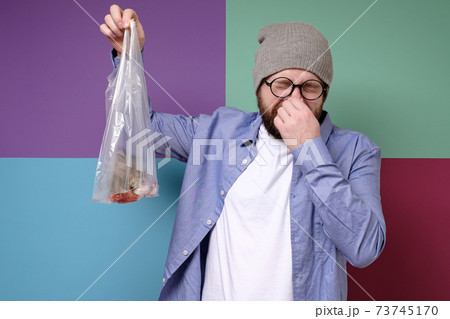 Man is holding a smelly fish in a transparent package, pinches fingers nose because of bad smell and 73745170