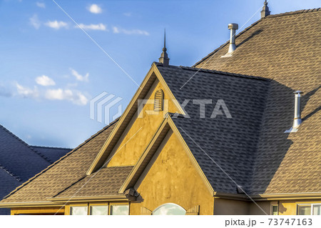 Close up of the roof and brown wall of a home against blue sky on a sunny day 73747163
