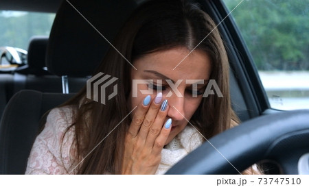 Sad and tired woman leaning her head on the steering wheel, crying while sitting in the car. 73747510
