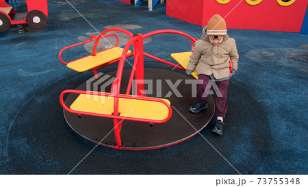 Little boy in warm hat and jacket rides on merry-go-round Little boy in warm hat and jacket rides on merry-go-round 73755348