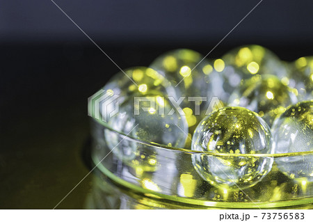 黒を背景に透明な皿の中に入った黄色に染まったガラス球の写真素材