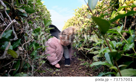 Funny girl in stylish jacket plays between bushes in park Funny girl in stylish jacket plays between bushes in park 73757001