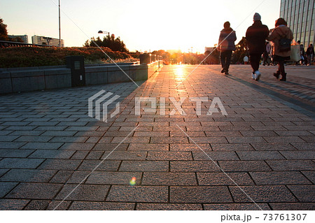 夕焼けに急ぐ人の波と地面に映る夕日の写真素材