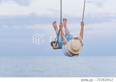 Child soars high riding on swing. Rope swing over the sea Child soars high riding on swing. Rope swing over the sea 73762912