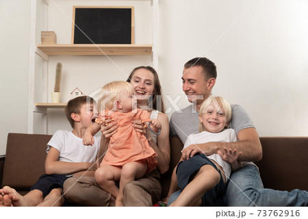 Mom dad and three children are sitting together on couch. Big friendly family 73762916