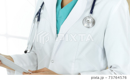 Unknown female doctor sitting and using tablet computer in clinic, close-up. Medicine concept Unknown female doctor sitting and using tablet computer in clinic, close-up. Medicine concept 73764576