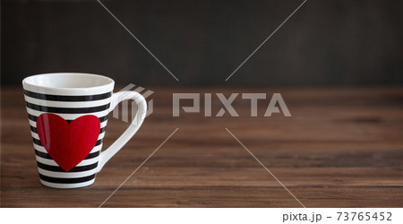 Stripy black and white cup with red heart on wooden background. Valentine's Day Cup. Love Concept 73765452