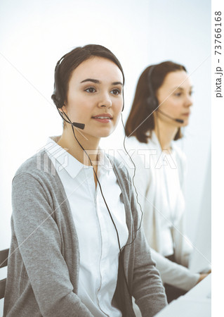 Call center. Casual dressed woman working in headset with diverse colleagues at office. Business concept 73766168