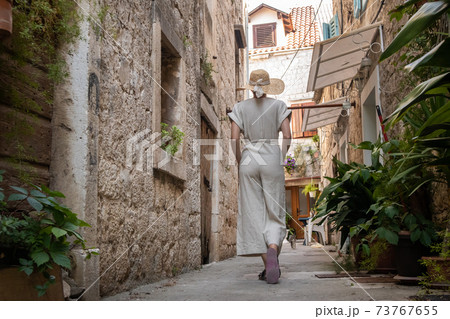 Rear view of beautiful blonde young female traveler wearing straw sun hat sightseeing and enjoying summer vacation in an old traditional costal town at Adriatic cost, Croatia Rear view of beautiful blonde young female traveler wearing straw sun hat sightseeing and enjoying summer vacation in an old traditional costal town at Adriatic cost, Croatia 73767655