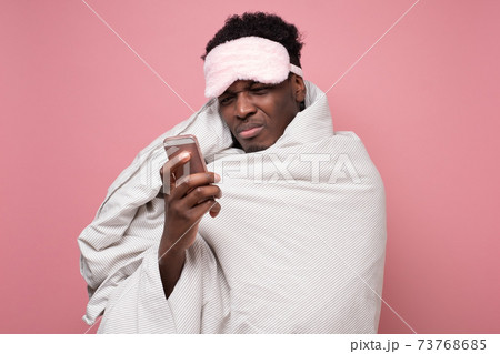 Sleepy young man under a blanket with phone waking up 73768685