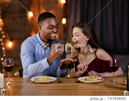 Romantic Interracial Couple Having Fun During Dinner In Restaurant, Eating Spaghetti Together 73769600