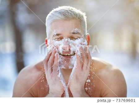 Positive mature guy washing his face with snow, standing with bare torso at winter forest, developing resistance to cold 73769601