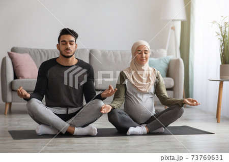 Prenatal Yoga Concept. Pregnant religious muslim couple meditating together at home Prenatal Yoga Concept. Pregnant religious muslim couple meditating together at home 73769631