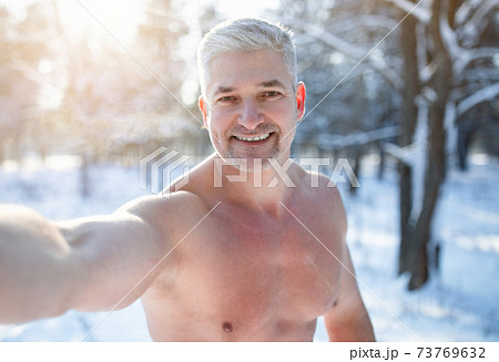 Smiling mature guy with naked torso taking selfie at snowy winter park. Seasonal pastimes Smiling mature guy with naked torso taking selfie at snowy winter park. Seasonal pastimes 73769632