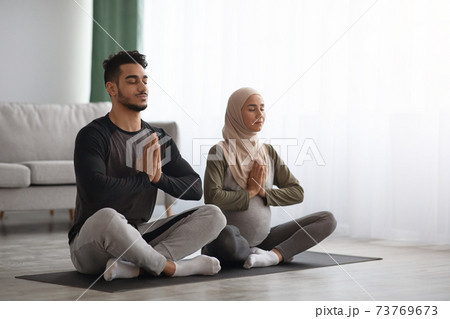 Pregnant Muslim Woman In Hijab Meditating Together With Her Husband At Home Pregnant Muslim Woman In Hijab Meditating Together With Her Husband At Home 73769673