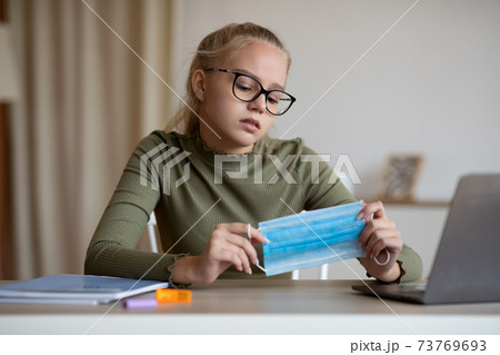 School girl holding face mask, sitting in front of laptop School girl holding face mask, sitting in front of laptop 73769693