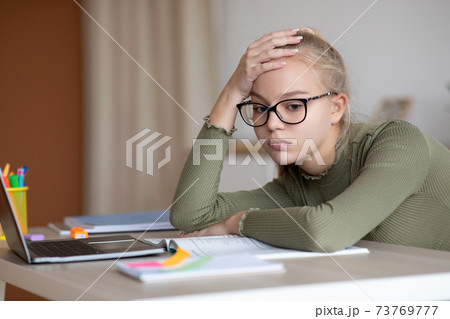 Bored teen girl sitting at home with book, doing homework Bored teen girl sitting at home with book, doing homework 73769777