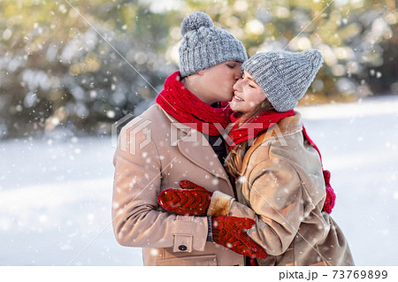 Loving man kissing his happy girlfriend over winter forest Loving man kissing his happy girlfriend over winter forest 73769899
