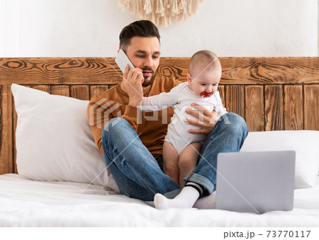 Father Talking On Phone Caring For Baby Working At Home Father Talking On Phone Caring For Baby Working At Home 73770117