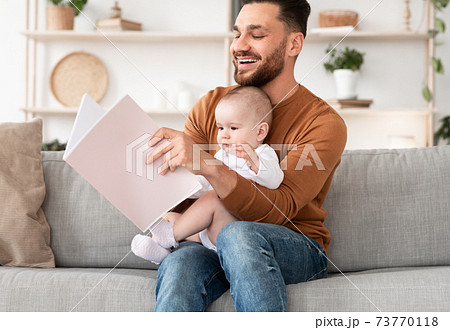 Young Father Reading Book For Little Baby Sitting At Home Young Father Reading Book For Little Baby Sitting At Home 73770118