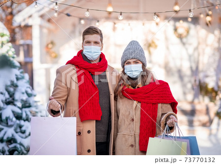 Couple in face masks holding shopping bags on winter day Couple in face masks holding shopping bags on winter day 73770132