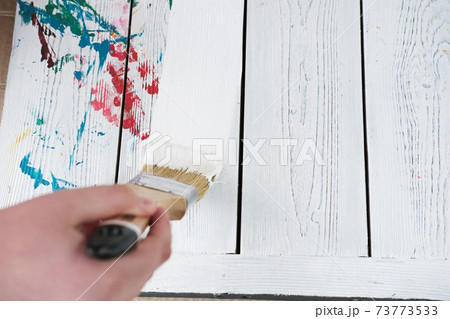 human hand holding brush painting white color on a white wooden table. 73773533