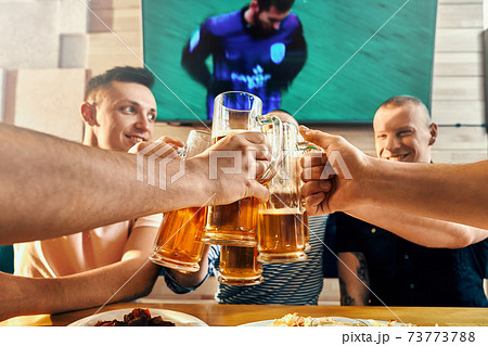 Men keeping glasses of beer and toasting in cafe 73773788
