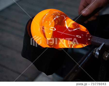 Shaping the red melted glass on  glassblowing pipe 73776043