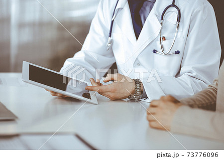 Unknown male doctor and patient woman discussing something while sitting in clinic and using tablet computer. Best medical service in hospital, medicine, pandemic stop Unknown male doctor and patient woman discussing something while sitting in clinic and using tablet computer. Best medical service in hospital, medicine, pandemic stop 73776096
