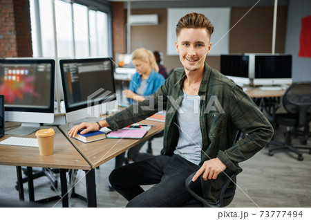 Smiling male IT specialist sits at the table Smiling male IT specialist sits at the table 73777494