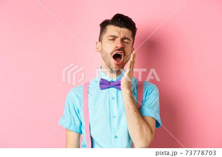 Image of tired guy in bow-tie yawning with opened mouth and closed eyes, standing sleepy, feeling fatigue, standing over pink background 73778703