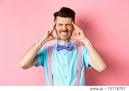 Image of man with headache touching head temples, grimacing from painful migraine, clench teeth, standing sick on pink background 73778707