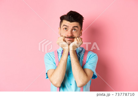 Silly young man leaning on hands and looking up, dreaming of something, imaging things on pink background 73778710