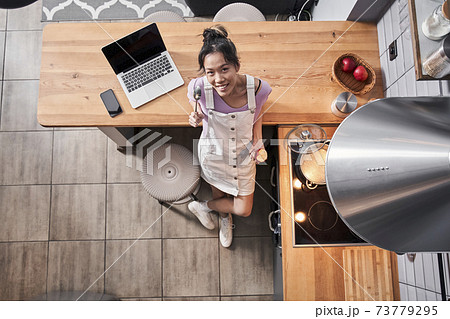 Woman standing at kitchen with a ladle spoon while eating 73779295