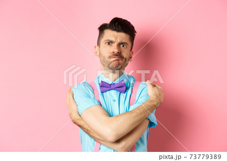 Timid guy embracing own body, comforting himself and looking offended, sulking at you, standing insulted and sad on pink background 73779389