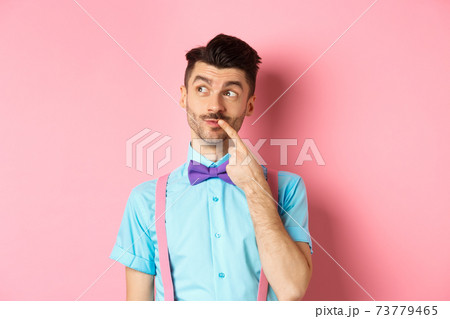 Image of handsome funny man in bow-tie looking thoughtful left and touching lip, thinking what to choose, making decision, standing over pink background 73779465